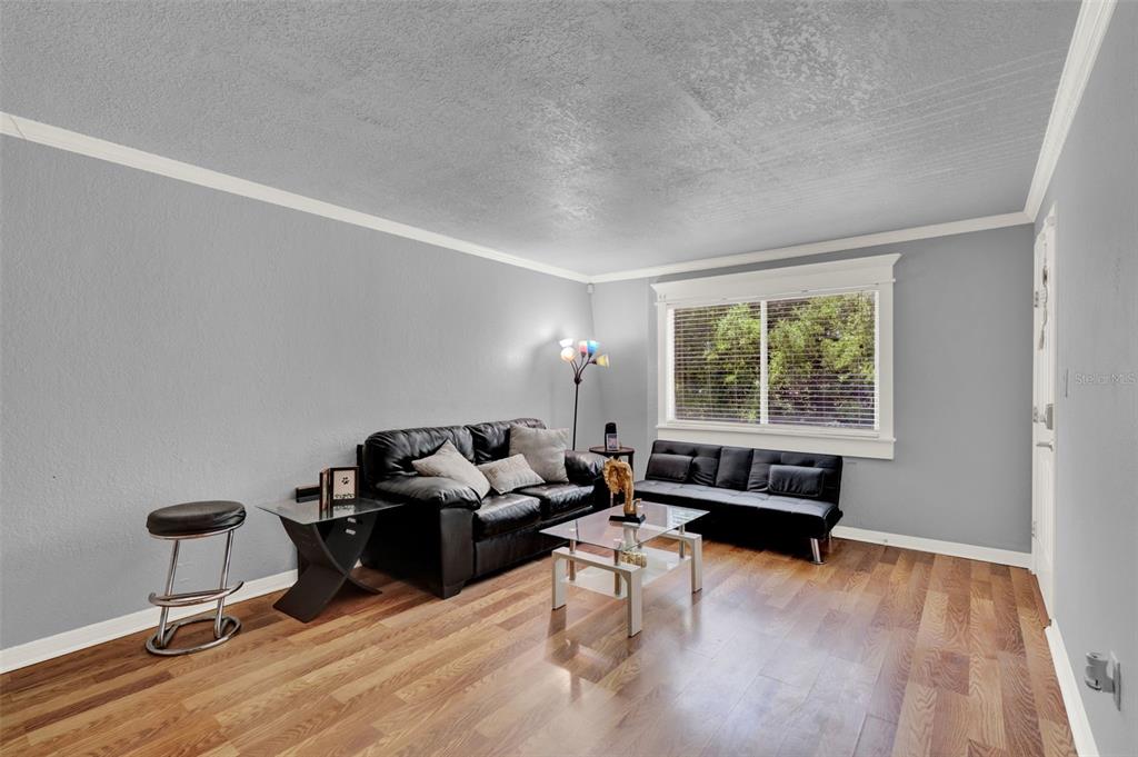 A living room features gray walls, wood flooring, a black sofa, and a glass coffee table — 1940 CONWAY UNIT 8, ORLANDO, FL