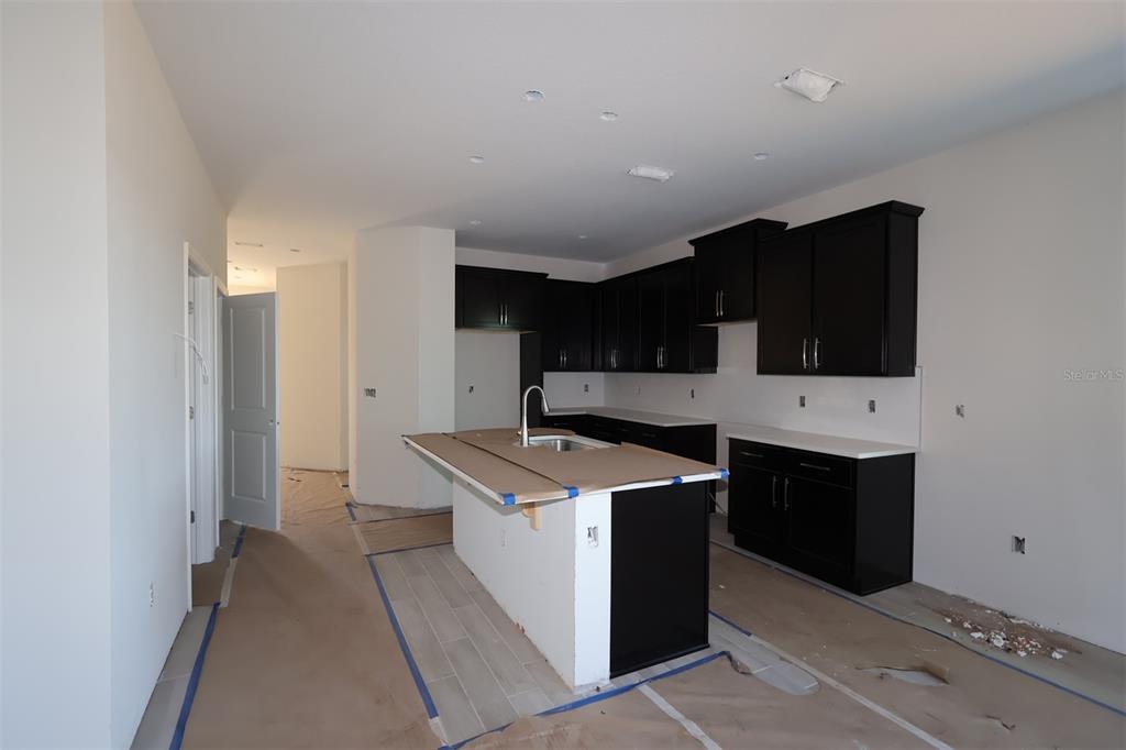 An unfinished kitchen features dark cabinets, white countertops, a center island, and protective floor paper — 5192 CENTER LAKE RANCH BOULEVARD, ST CLOUD, FL