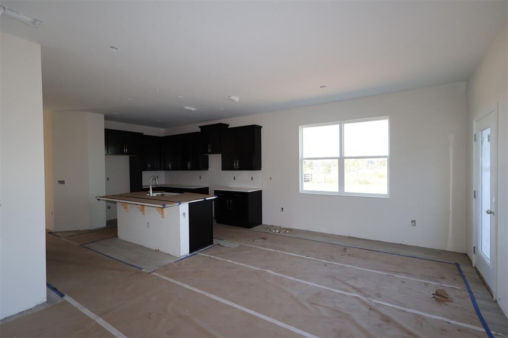 An unfinished kitchen features dark cabinets, a center island with a sink, and paper-covered floors — 5192 CENTER LAKE RANCH BOULEVARD, ST CLOUD, FL