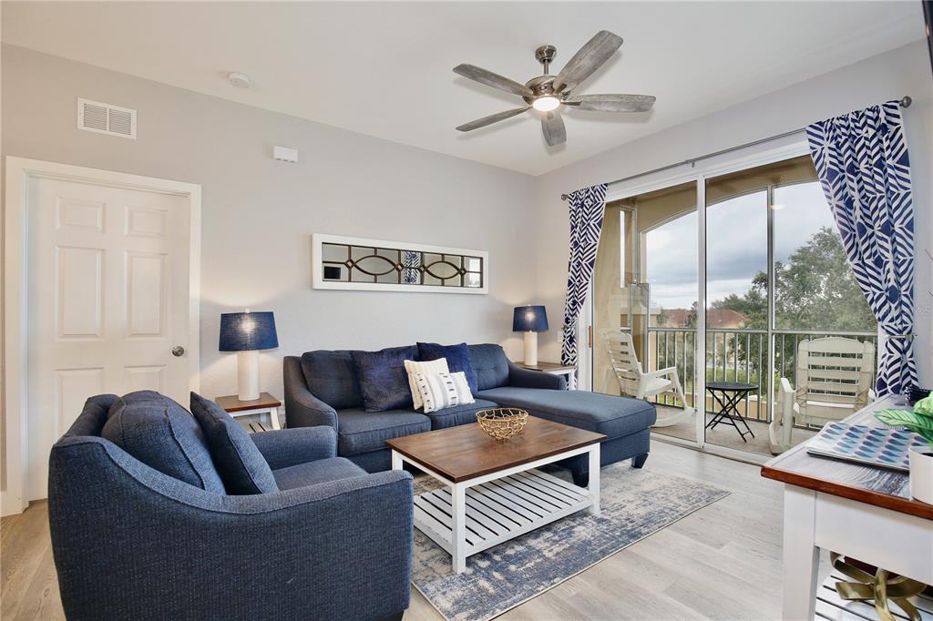 A living room features a blue sectional sofa, a coffee table, and a sliding glass door — 2821 ALMATON LOOP UNIT 301, KISSIMMEE, FL