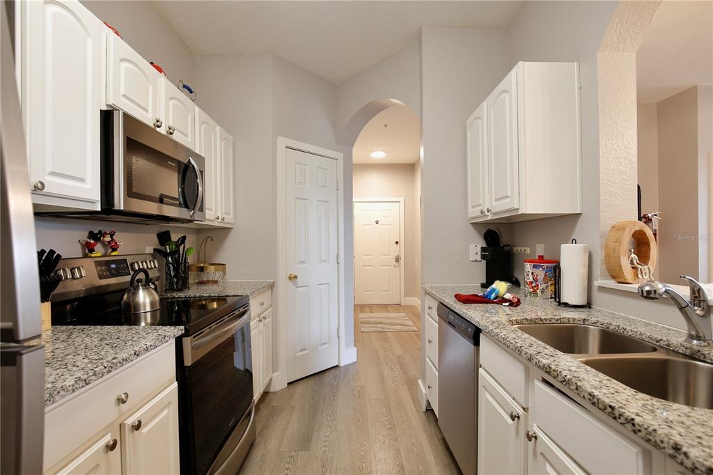 A galley kitchen features white cabinets, granite countertops, stainless steel appliances, and wood-look flooring — 2821 ALMATON LOOP UNIT 301, KISSIMMEE, FL