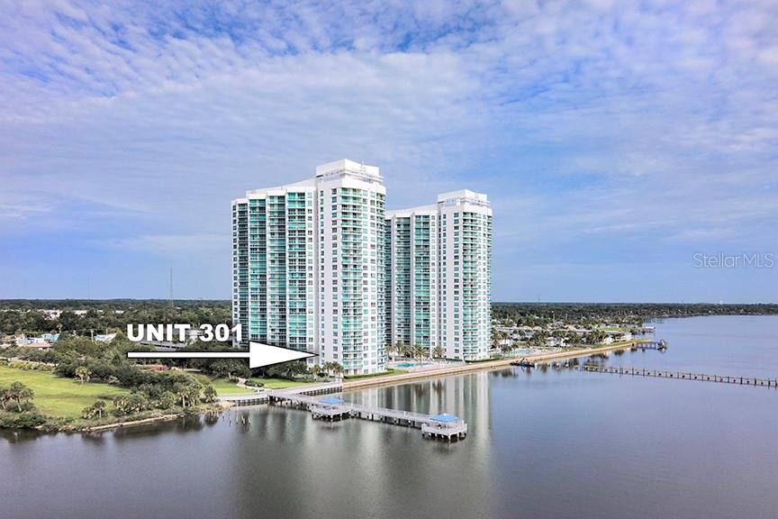 An aerial view shows a tall, multi-story residential building situated along a waterfront with docks — 231 RIVERSIDE DRIVE UNIT 301-1, HOLLY HILL, FL