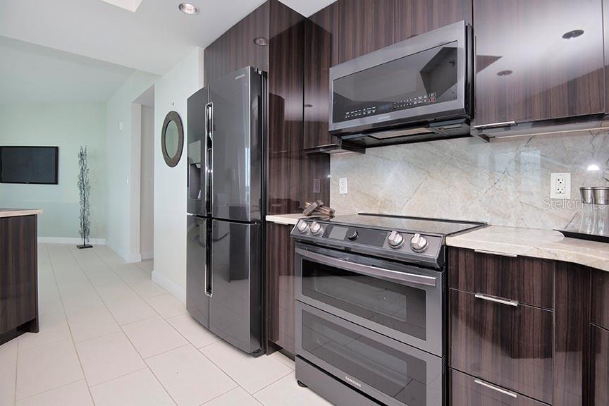 A modern kitchen features dark wood cabinetry, stainless steel appliances, and a light stone backsplash — 231 RIVERSIDE DRIVE UNIT 301-1, HOLLY HILL, FL