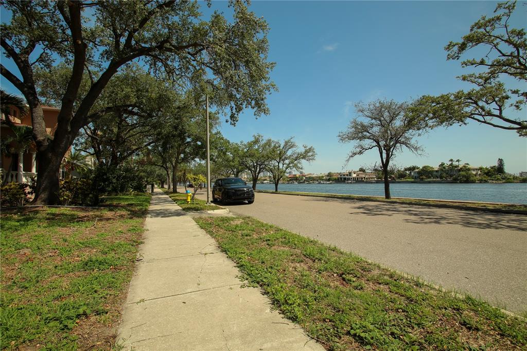 A sidewalk runs along a road beside a waterway lined with trees and houses — 424 CHANNEL DRIVE, TAMPA, FL