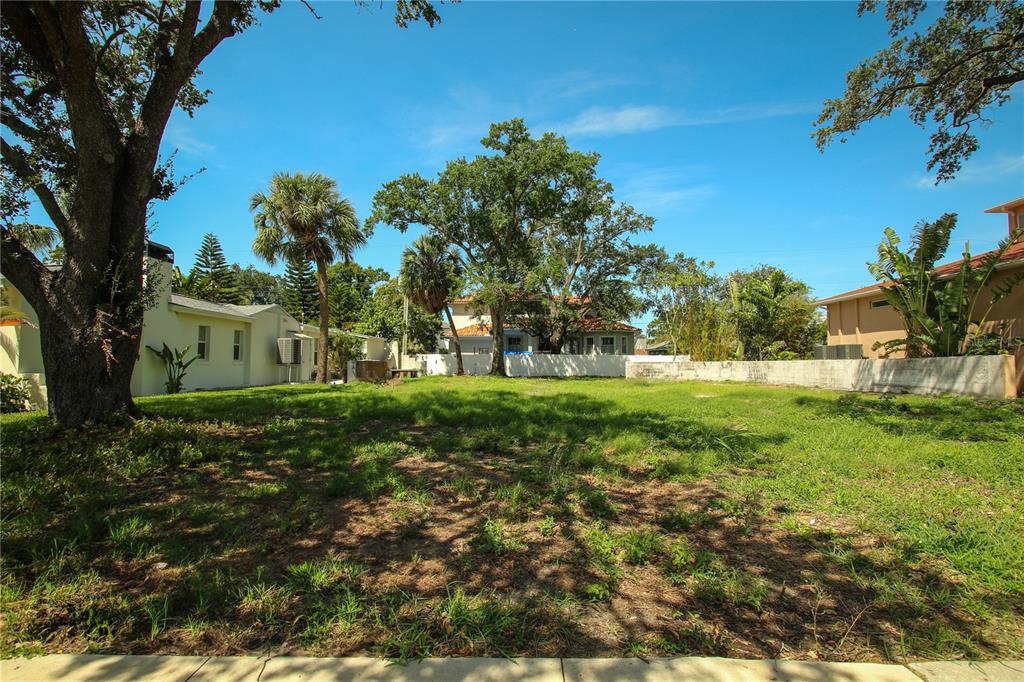 A vacant, grassy residential lot is surrounded by trees, neighboring houses, and a concrete wall — 424 CHANNEL DRIVE, TAMPA, FL
