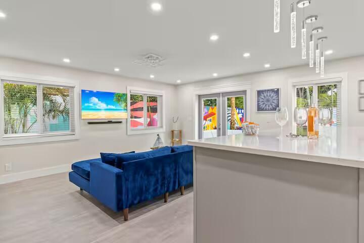 A modern living room features a blue velvet sectional, a wall-mounted television, and kitchen island — 322 NW 4th Avenue, Delray Beach FL 33444, DELRAY BEACH, FL
