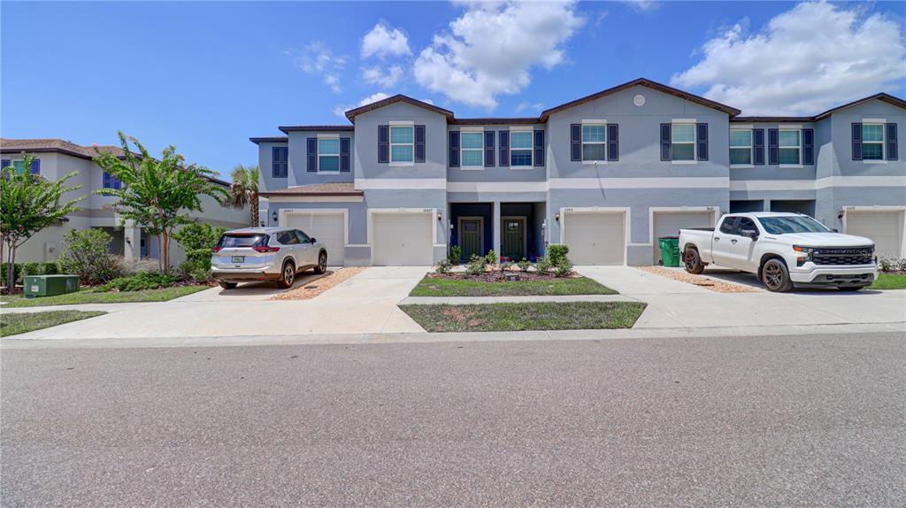 A row of two-story townhouses with attached garages and driveways under a blue sky — 36427 GARDEN WALL WAY, ZEPHYRHILLS, FL