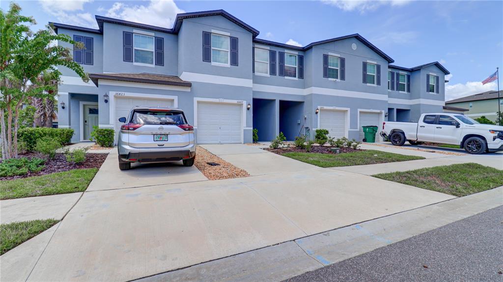 A row of blue two-story townhouses features attached garages and concrete driveways under a blue sky — 36427 GARDEN WALL WAY, ZEPHYRHILLS, FL
