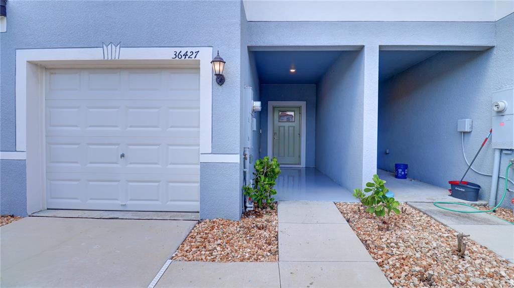 The exterior of a house features a garage, a covered entryway, and a concrete walkway — 36427 GARDEN WALL WAY, ZEPHYRHILLS, FL