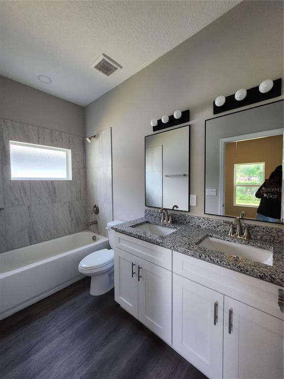 A bathroom features a double vanity with granite countertops, white cabinets, and a tiled tub-shower — 5016 FINDERS COURT, TAMPA, FL