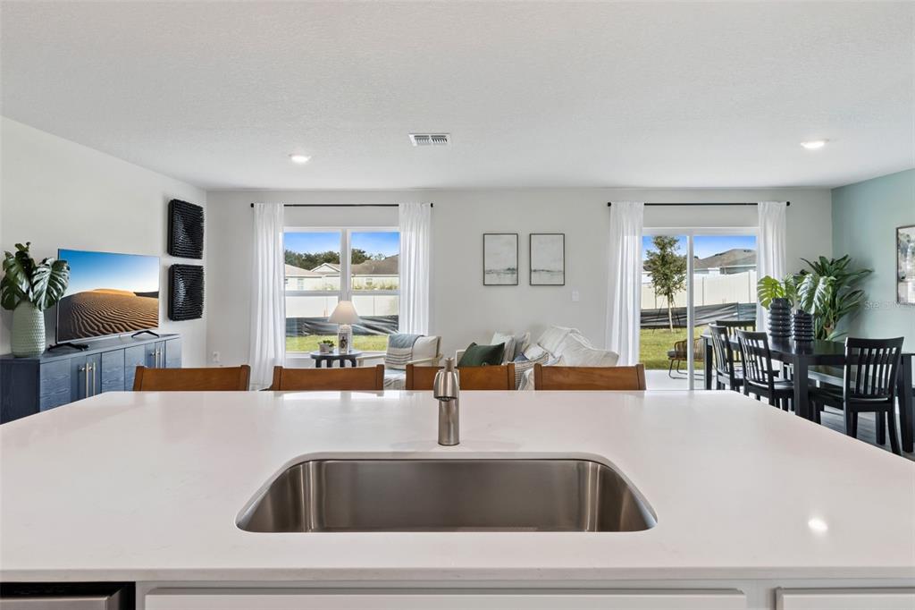A kitchen island with a stainless steel sink overlooks an open-concept living and dining area — 605 WALLABY LANE, KISSIMMEE, FL