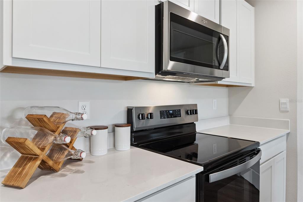 A kitchen features white cabinets, a stainless steel microwave, a black stove, and quartz countertops — 605 WALLABY LANE, KISSIMMEE, FL