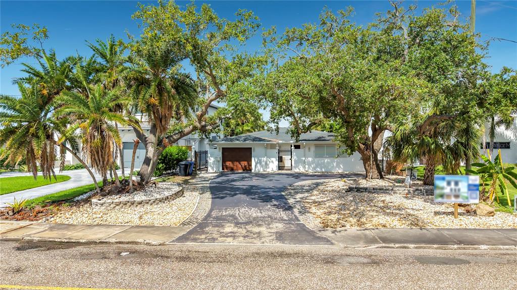 A single-story house with a paved driveway, a garage, and several large trees in front — 3800 SHORE ACRES BOULEVARD NE, ST PETERSBURG, FL