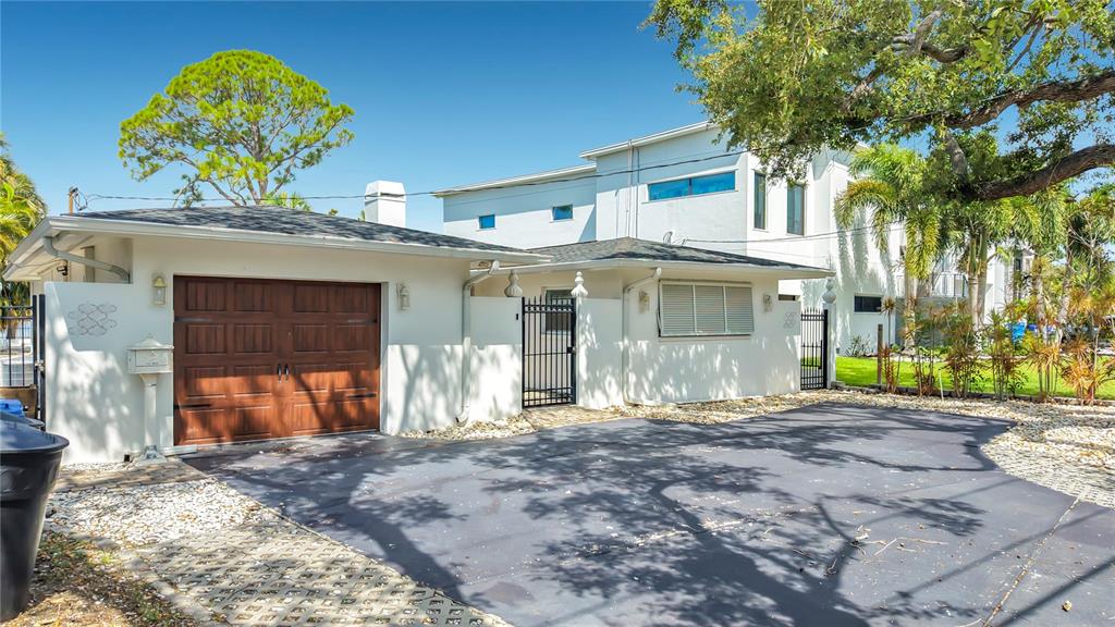 A white house with a brown garage door and a paved driveway under a tree — 3800 SHORE ACRES BOULEVARD NE, ST PETERSBURG, FL