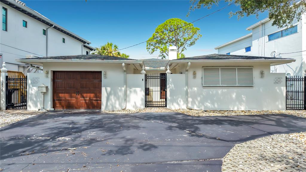 A single-story house with a brown garage door, white stucco walls, and a paved driveway — 3800 SHORE ACRES BOULEVARD NE, ST PETERSBURG, FL