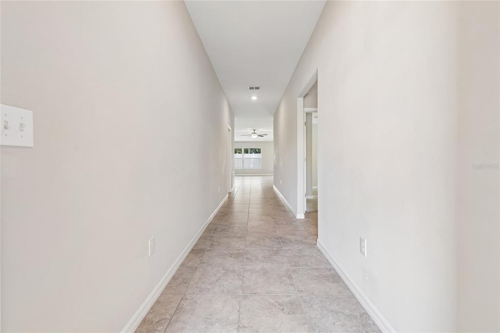 A long, tiled hallway with light-colored walls leads toward a windowed room in the distance — 3706 CAT MINT STREET, TAMPA, FL