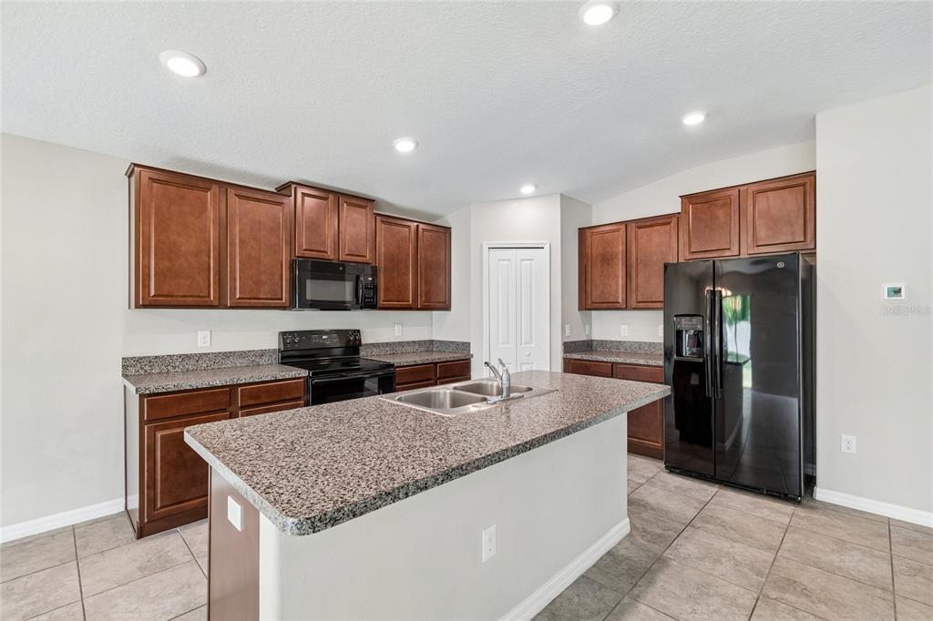 A kitchen features dark wood cabinets, granite countertops, an island with a sink, and appliances — 3706 CAT MINT STREET, TAMPA, FL