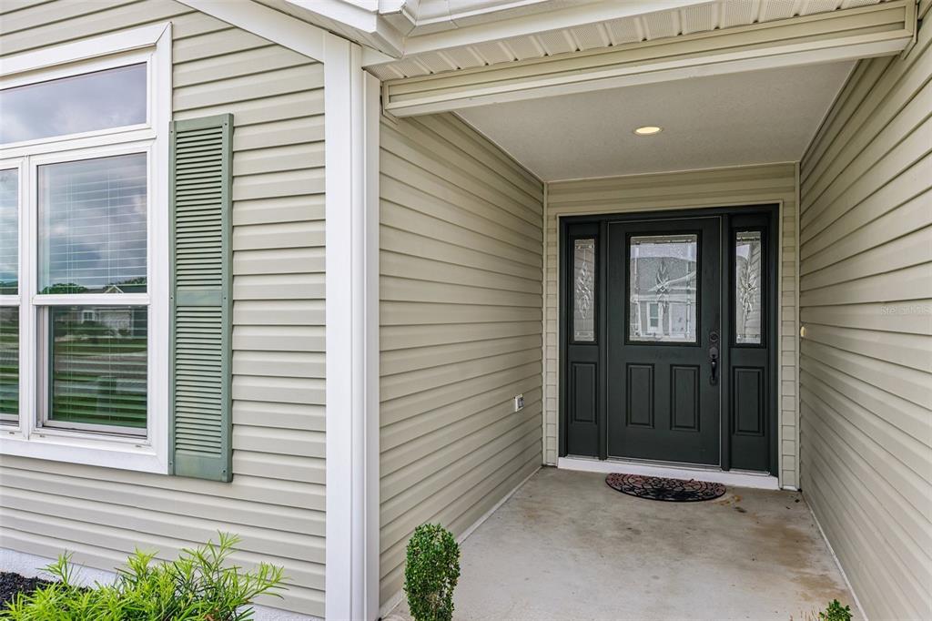 A covered entryway features light-colored horizontal siding, a dark front door, and a concrete porch — 3315 DZURO DRIVE, OXFORD, FL