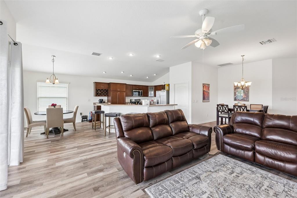 An open-concept living room, dining area, and kitchen feature wood-look flooring and brown leather furniture — 3315 DZURO DRIVE, OXFORD, FL