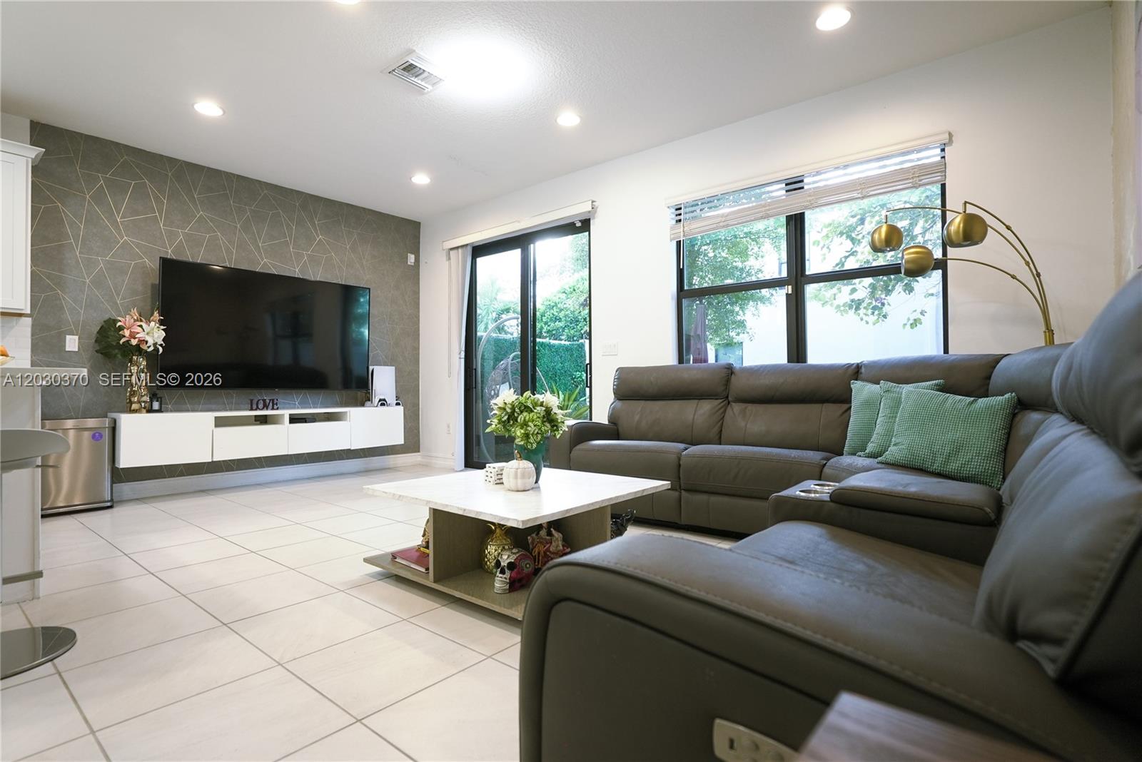A living room features a geometric accent wall, a wall-mounted media console, and a sectional sofa — 10111 Akenside Dr # 10111, Boca Raton FL 33428, BOCA RATON, FL