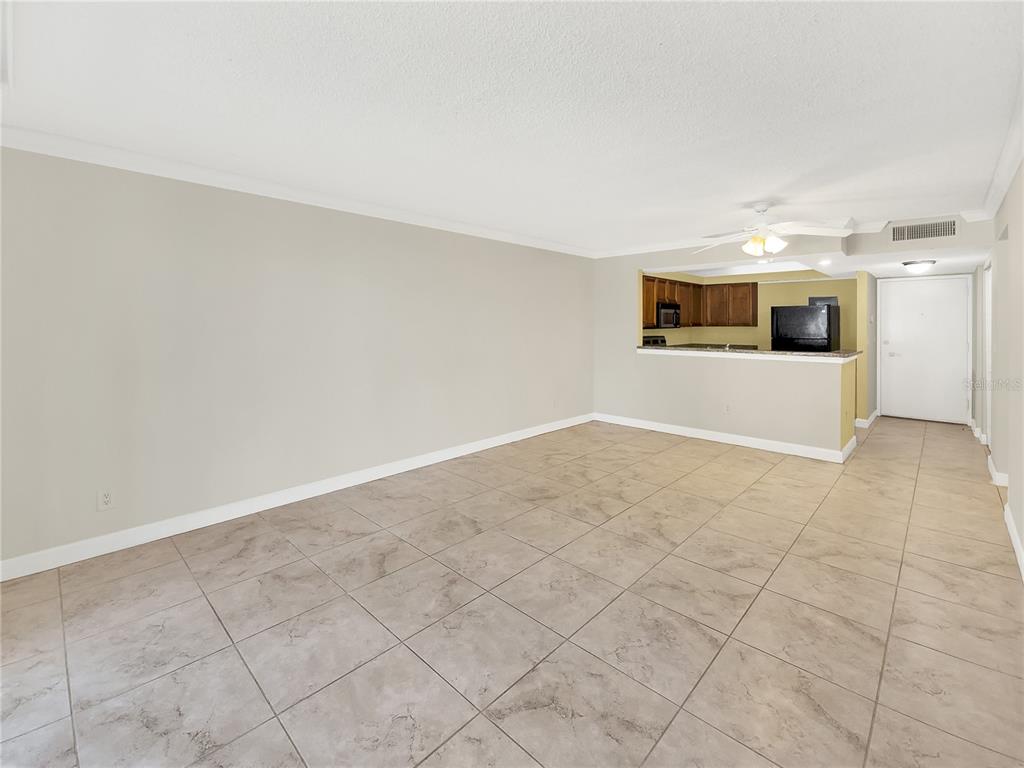 An open-concept living area with beige tile flooring, neutral walls, and an attached kitchen — 2700 COCONUT BAY LANE UNIT 419, SARASOTA, FL