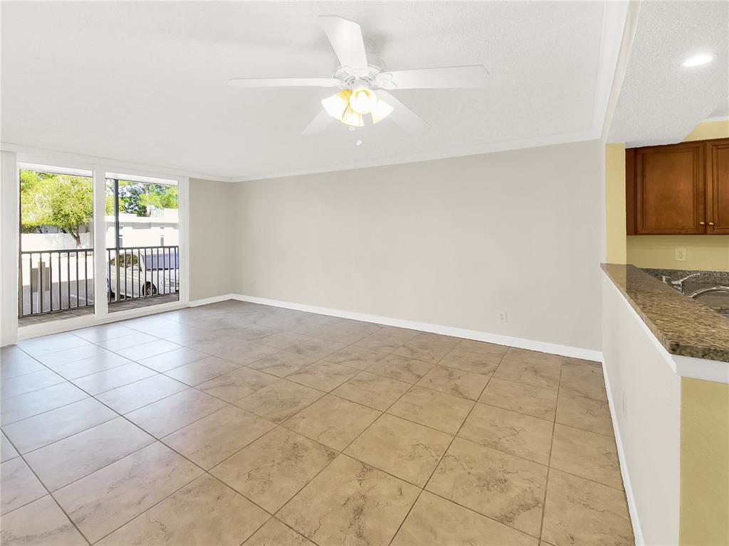 A living room with beige tile flooring, a ceiling fan, and a sliding glass door — 2700 COCONUT BAY LANE UNIT 419, SARASOTA, FL