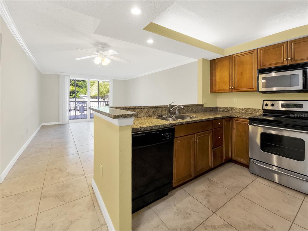 A kitchen with wood cabinets and granite countertops opens to a living area with tile — 2700 COCONUT BAY LANE UNIT 419, SARASOTA, FL