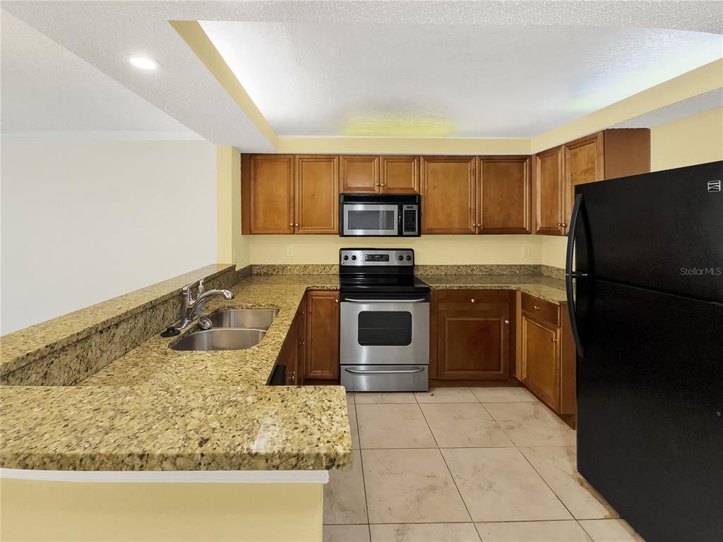 A kitchen features wood cabinets, granite countertops, stainless steel appliances, and a black refrigerator — 2700 COCONUT BAY LANE UNIT 419, SARASOTA, FL