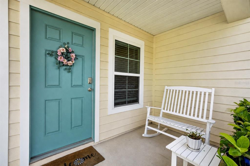 A teal front door with a floral wreath sits beside a white bench on a porch — 760 GRAND RESERVE DRIVE, BUNNELL, FL