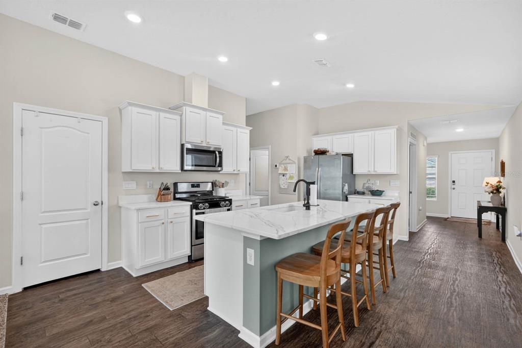 A kitchen with white cabinets, a marble-topped island, stainless steel appliances, and dark wood flooring — 760 GRAND RESERVE DRIVE, BUNNELL, FL