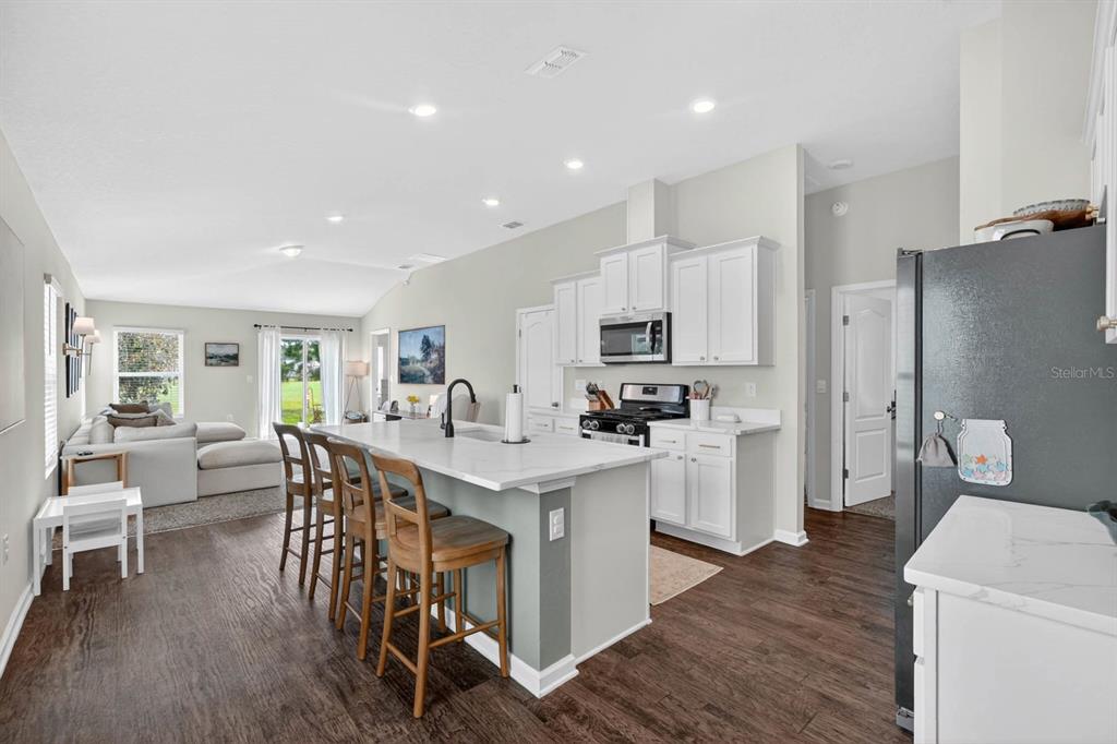 A kitchen with white cabinets, a marble-topped island, and bar stools overlooks a living area — 760 GRAND RESERVE DRIVE, BUNNELL, FL