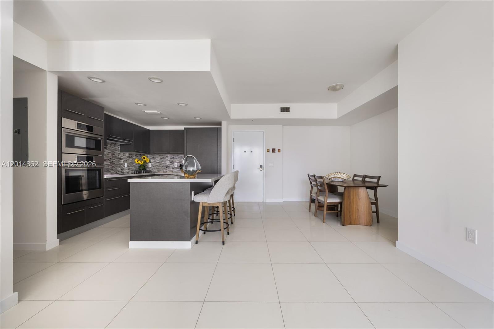 A modern kitchen with dark cabinetry and a central island sits beside a dining area — 7825 NW 107th Ave # 419, Doral FL 33178, DORAL, FL