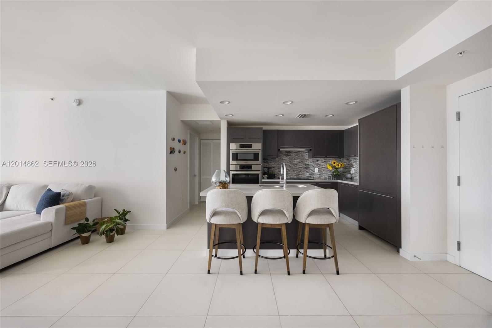 A modern kitchen features dark cabinetry, a central island with three stools, and tile flooring — 7825 NW 107th Ave # 419, Doral FL 33178, DORAL, FL