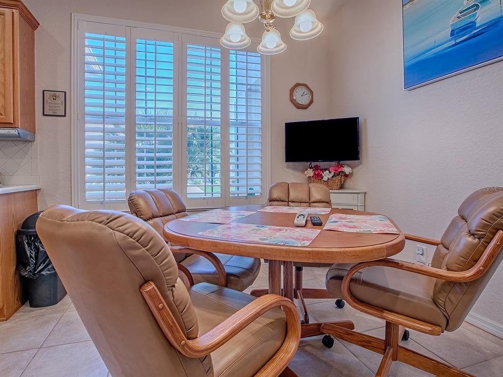 A dining area features a round wooden table, four tan chairs, and plantation shutters — 13324 SE 91ST COURT ROAD, SUMMERFIELD, FL