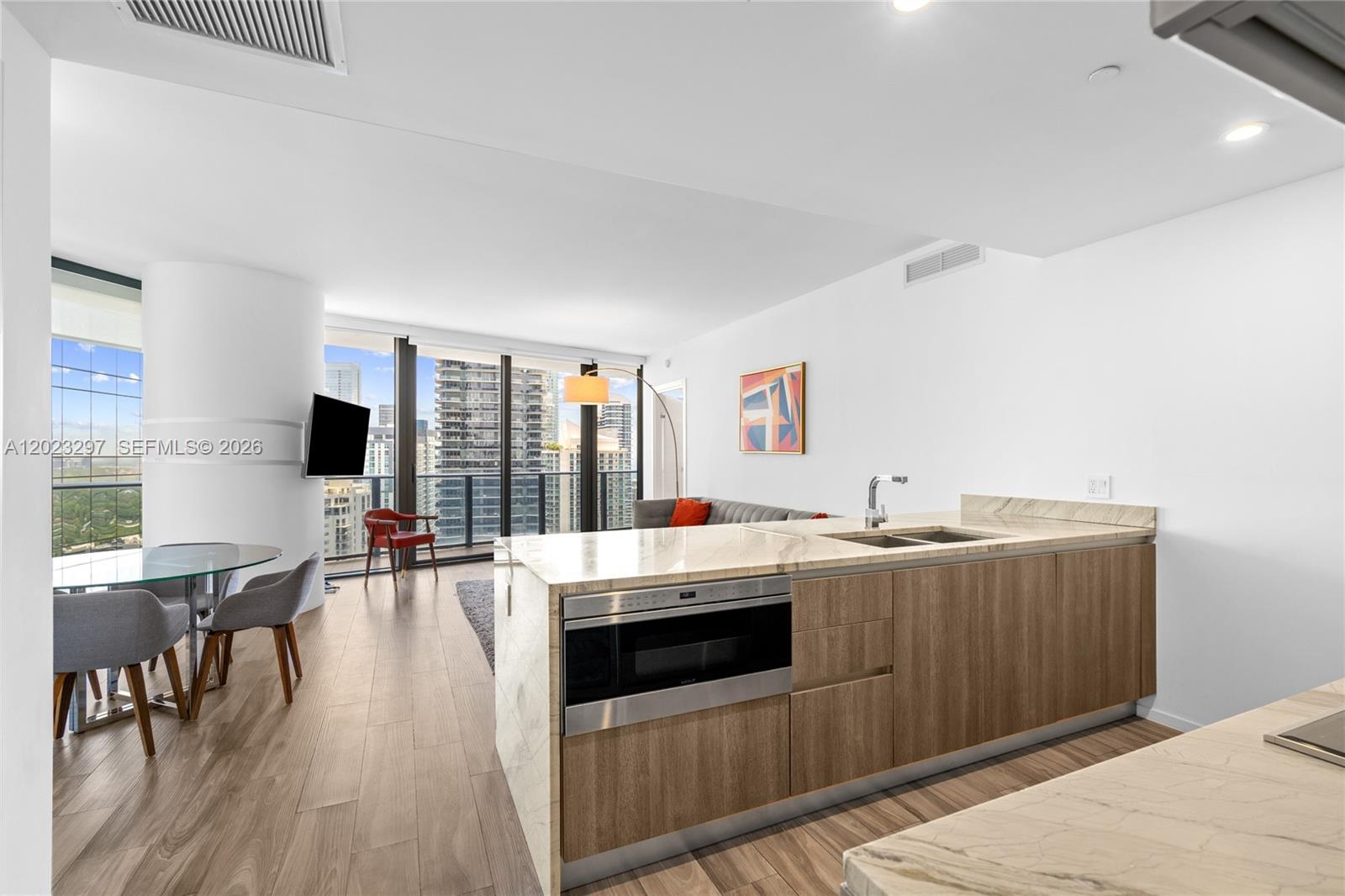 A modern kitchen island with a built-in microwave faces a dining area and city view — 801 S Miami Ave # 4104, Miami FL 33130, MIAMI, FL