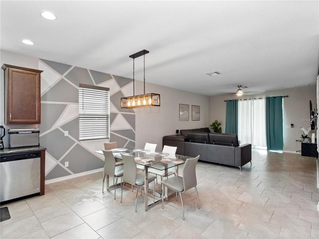 A dining area with a geometric accent wall and glass table opens into a living room — 2160 PRESTON LANE, KISSIMMEE, FL