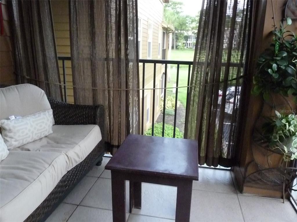 A covered balcony features a wicker sofa, a small wooden table, and brown privacy curtains — 400 SUMMIT RIDGE PLACE UNIT 216, LONGWOOD, FL