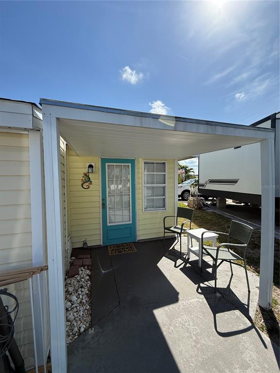 A covered patio with a teal door, two chairs, and a small table — 1475 FLAMINGO DRIVE UNIT 117, ENGLEWOOD, FL