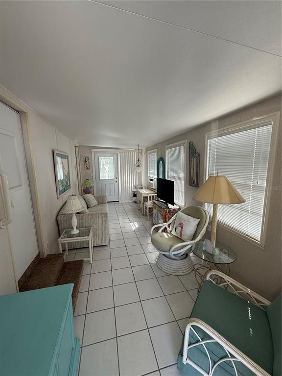 A sunroom features white tiled flooring, a sofa, two armchairs, and a television on a stand — 1475 FLAMINGO DRIVE UNIT 117, ENGLEWOOD, FL