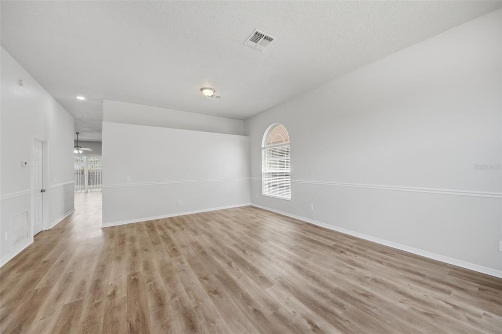 An empty room with light wood-look flooring, white walls, chair rail molding, and an arched window — 3724 BECONTREE PLACE, OVIEDO, FL