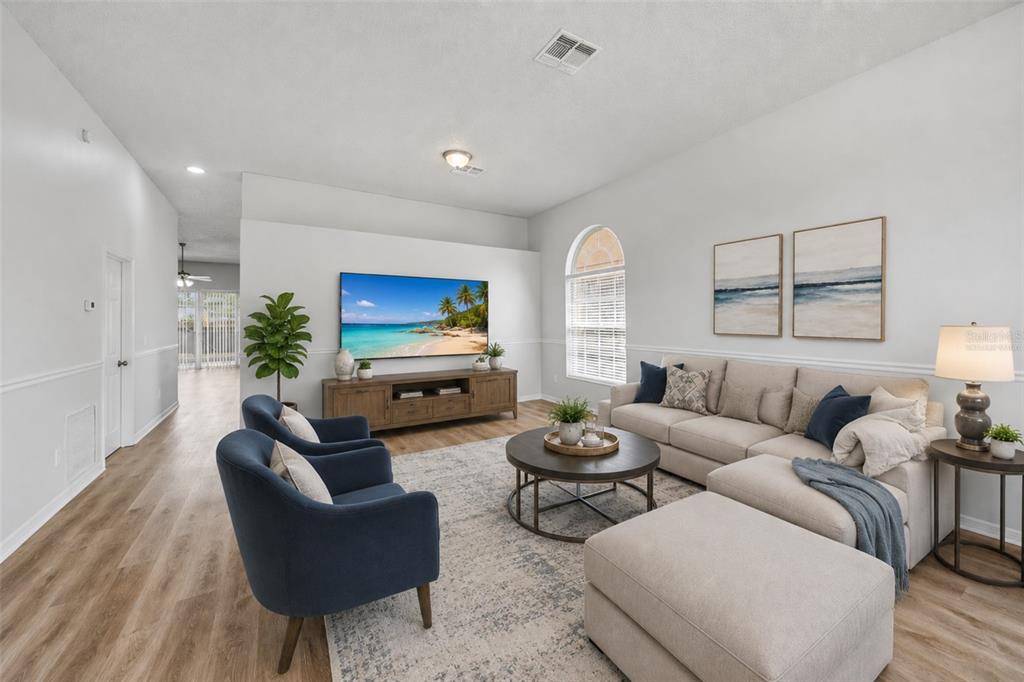 A living room features a sectional sofa, two blue armchairs, a television, and wood flooring — 3724 BECONTREE PLACE, OVIEDO, FL