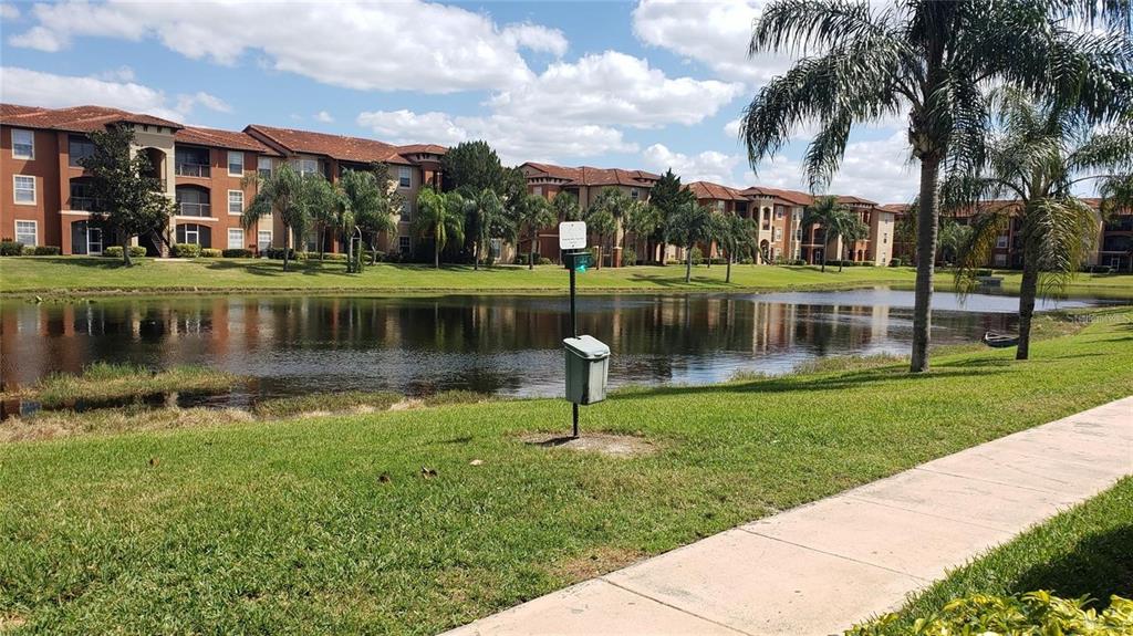 A view of a pond and apartment buildings from a grassy area with a sidewalk — 5566 METROWEST BOULEVARD UNIT 306, ORLANDO, FL