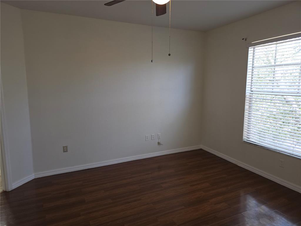 An empty bedroom features dark wood-look flooring, light-colored walls, a ceiling fan, and a window — 5566 METROWEST BOULEVARD UNIT 306, ORLANDO, FL