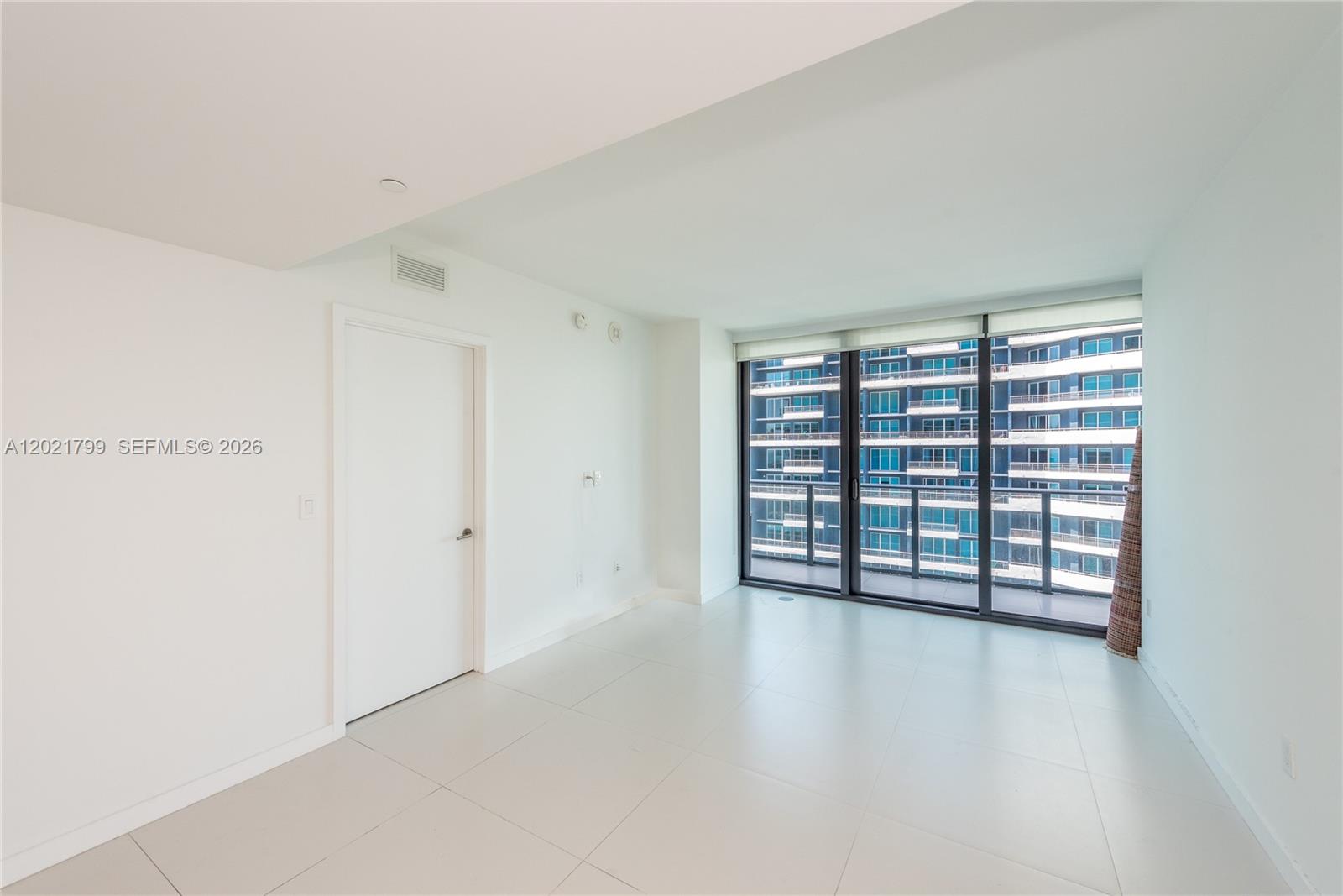 A bright, empty room features white walls, tile flooring, and floor-to-ceiling windows overlooking another building — 1300 S Miami Ave # 4709, Miami FL 33130, MIAMI, FL
