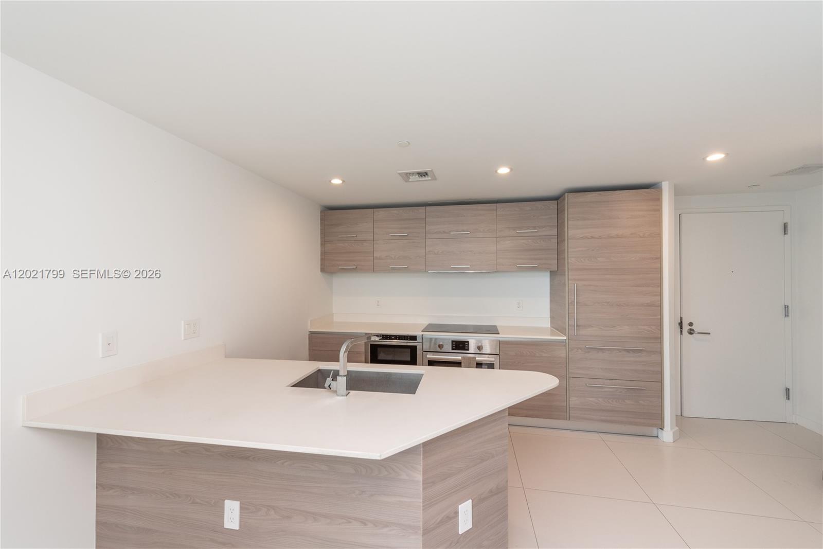 A modern kitchen features light wood cabinetry, a white countertop island, and stainless steel appliances — 1300 S Miami Ave # 4709, Miami FL 33130, MIAMI, FL