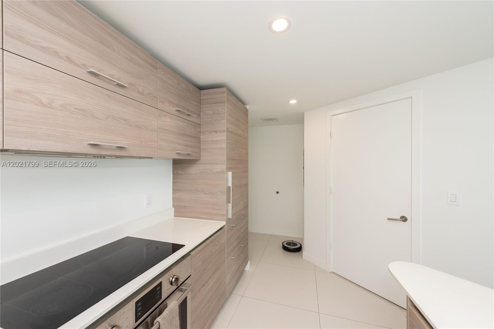A modern kitchen features light wood-grain cabinetry, a smooth cooktop, and white tile flooring — 1300 S Miami Ave # 4709, Miami FL 33130, MIAMI, FL