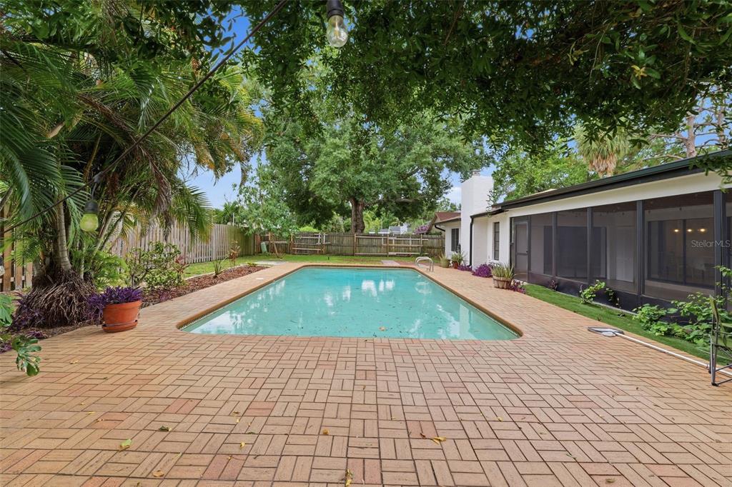 A backyard features a rectangular swimming pool surrounded by a brick patio and mature trees — 8307 VALLEJO PLACE, TAMPA, FL