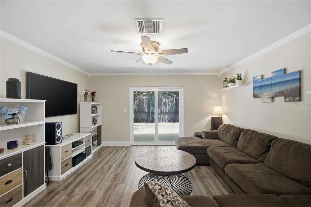 A living room features a brown sectional sofa, a round coffee table, and wood-look flooring — 2447 GROVE RIDGE DRIVE, PALM HARBOR, FL