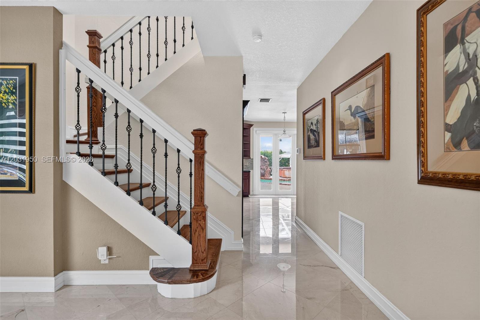 A foyer features a wooden staircase with iron railings, tiled floors, and framed wall art — 830 Hawthorn Ter, Weston FL 33327, WESTON, FL