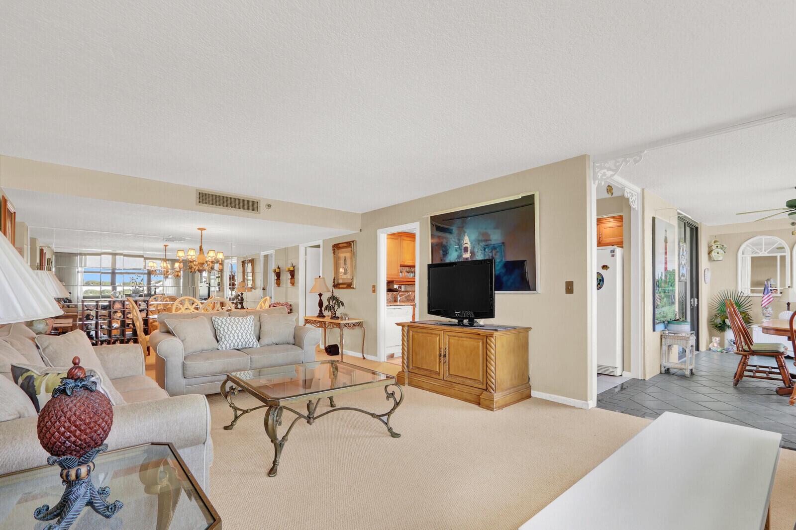 A living room with beige carpet, a sofa, a glass coffee table, and a television — 1648 Jupiter Cove Drive # 214, Jupiter FL 33469, JUPITER, FL